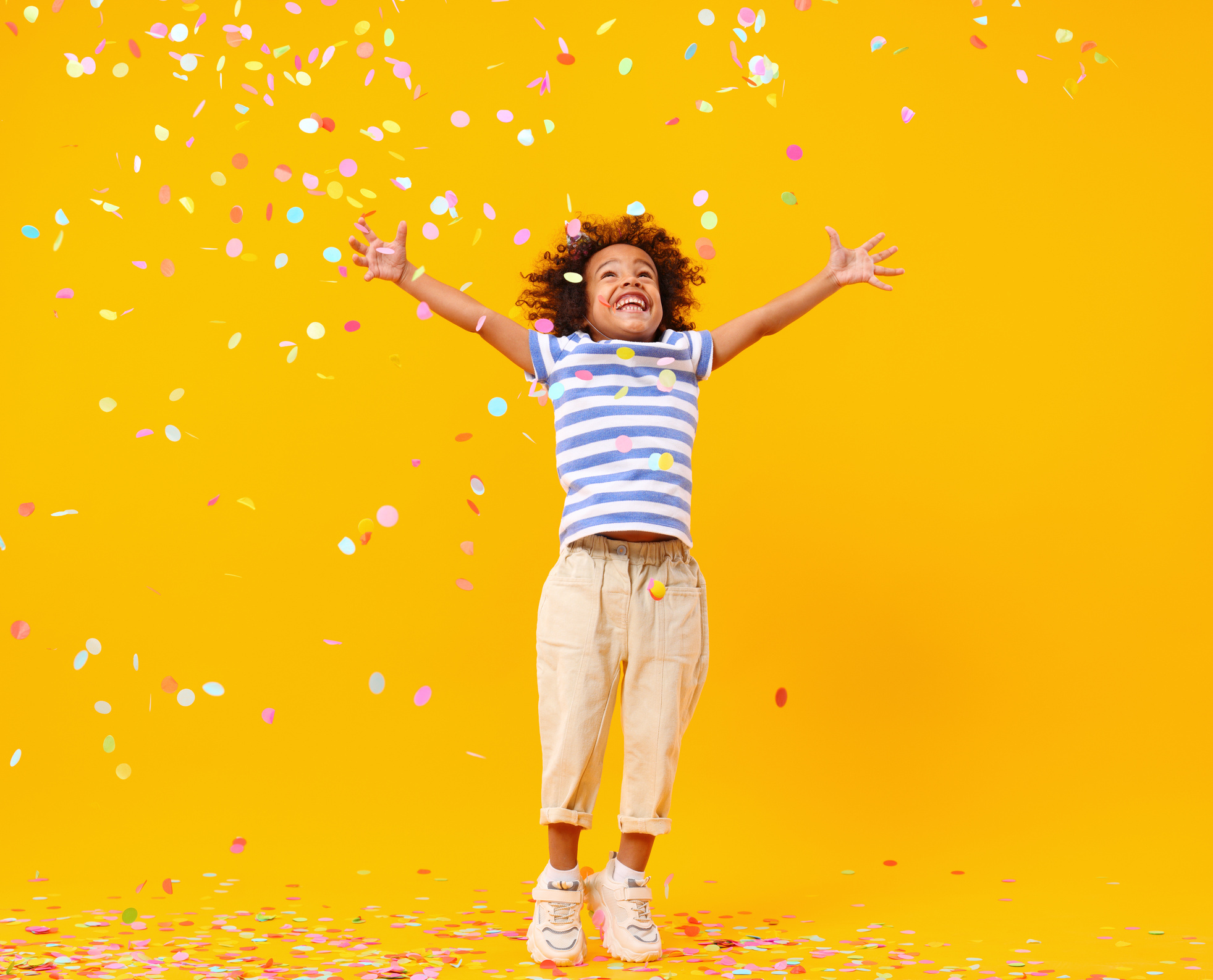 Excited African American kid jumping and catching confetti on birthday in studio